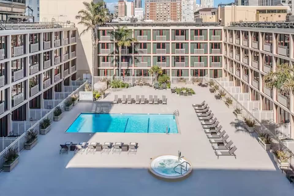 Modern resort courtyard with central rectangular pool, surrounding lounge chairs, and apartment buildings