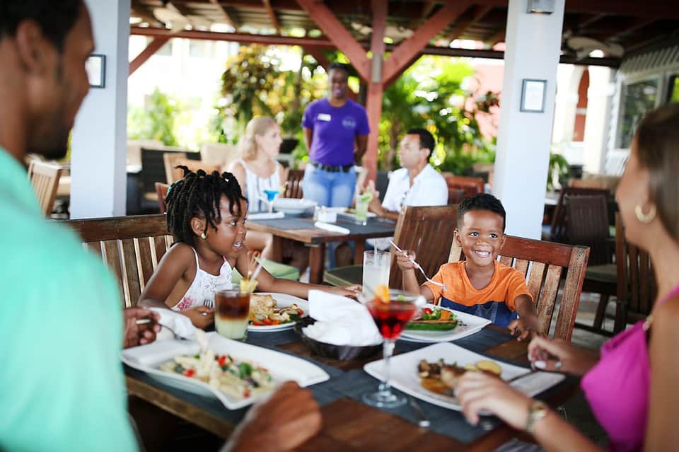 Family dining outdoors under covered pavilion with tropical plants and green surroundings
