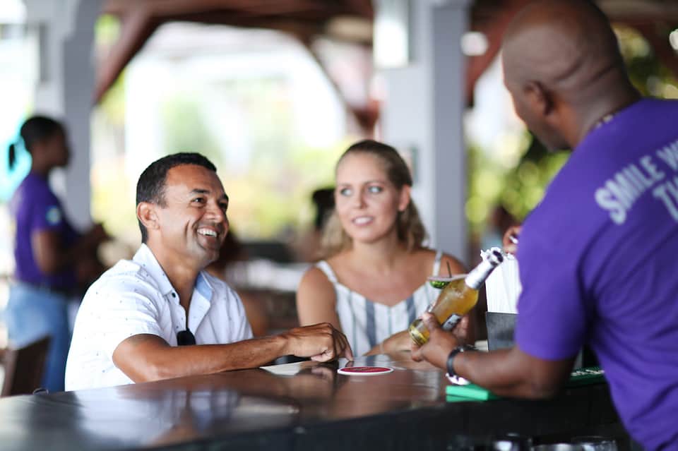 Staff member in purple shirt serving drinks to guests at an indoor bar or restaurant counter