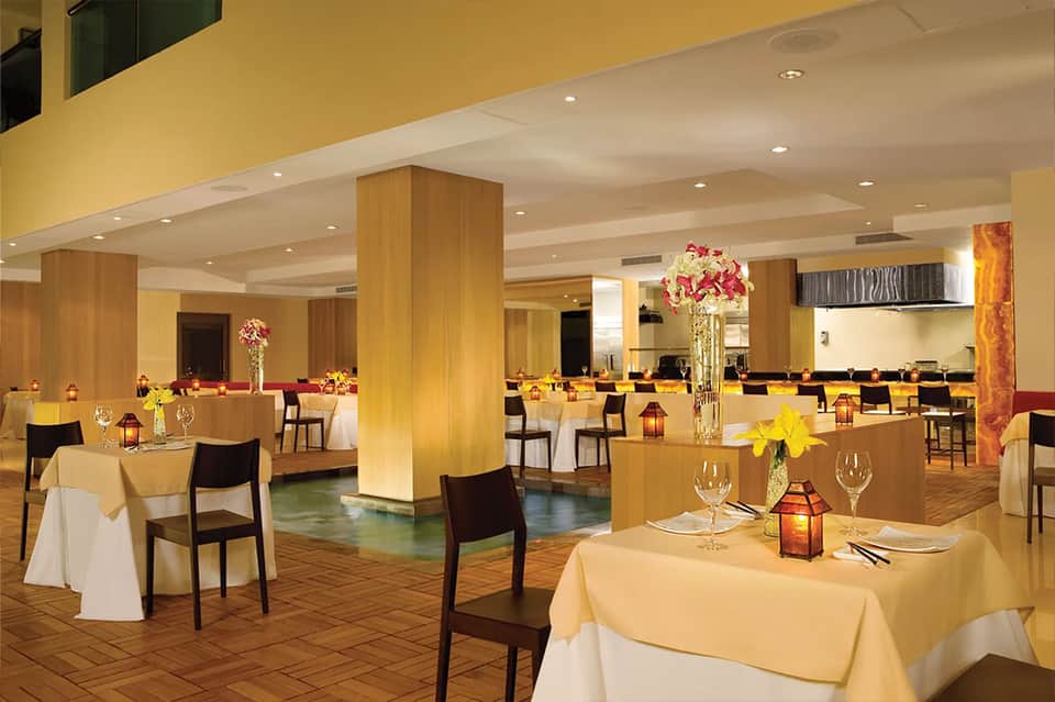 Elegant banquet hall with yellow walls, wood pillars, round tables with white linens, and centerpiece flowers