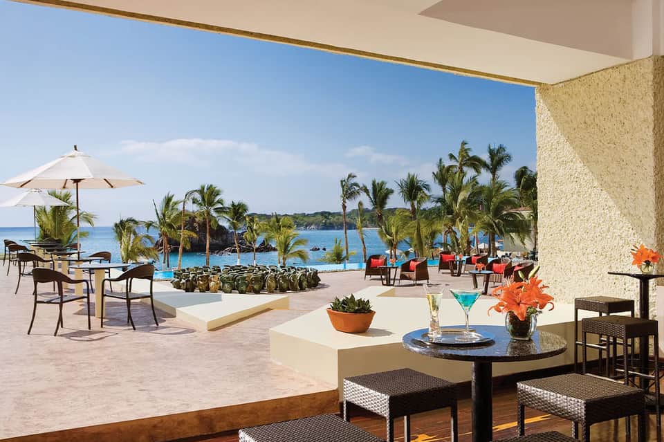 Resort terrace bar with cocktail, tropical flowers, and ocean view with palm trees