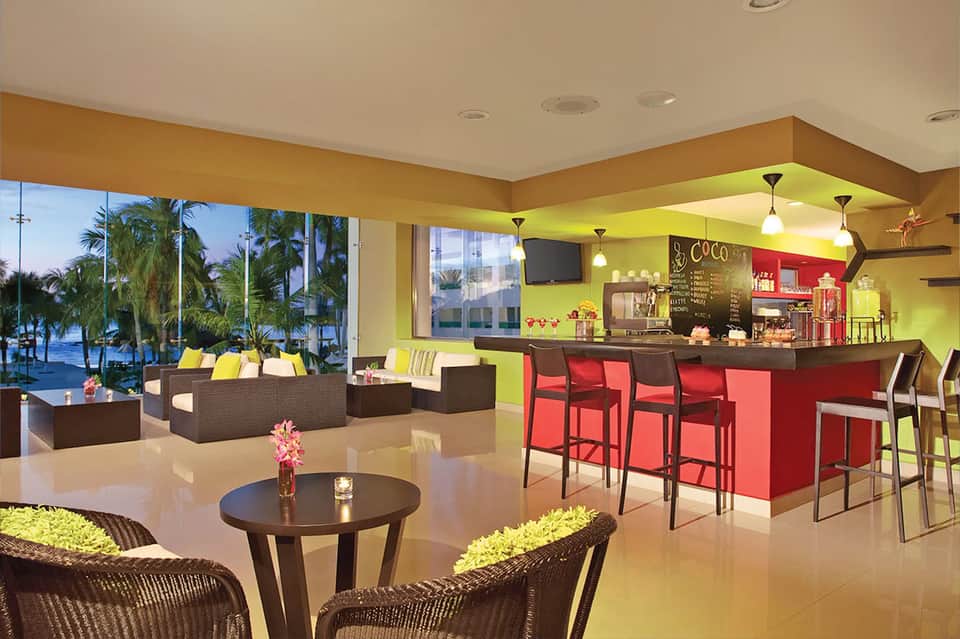 Vibrant hotel lobby with lime green ceiling, red bar, and ocean views through windows