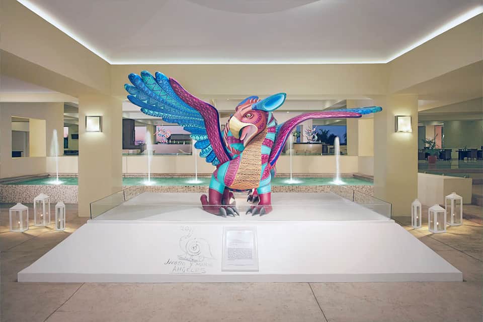 Exhibition space with colorful sculptural bird installation and white platform in bright minimalist interior