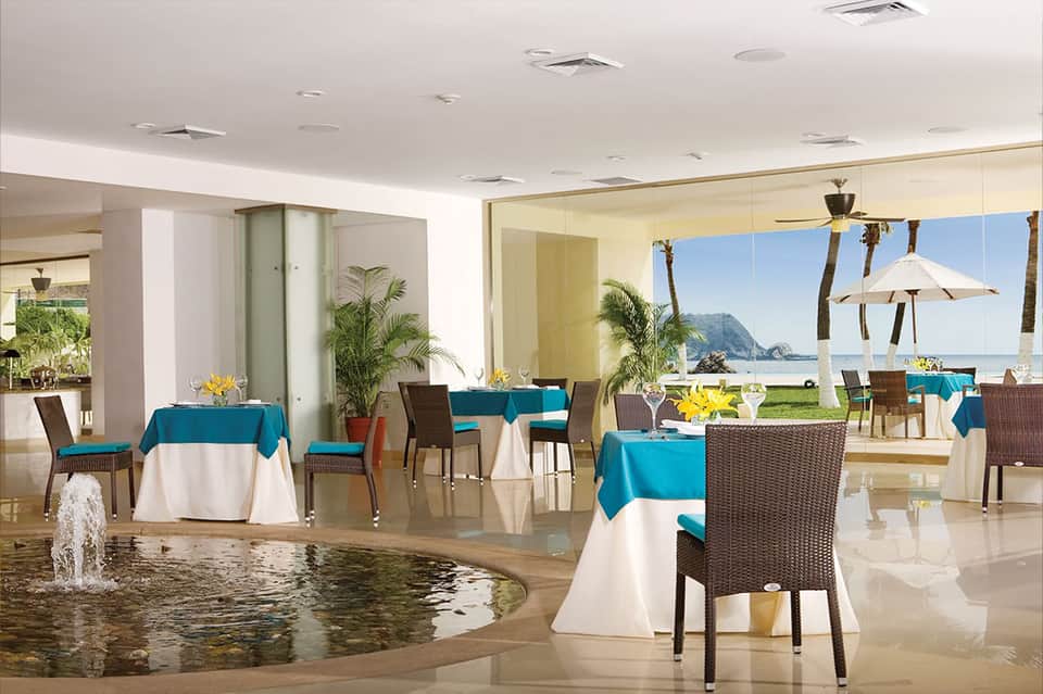 Upscale restaurant interior with ocean and mountain views, teal tablecloths, and coastal scenery