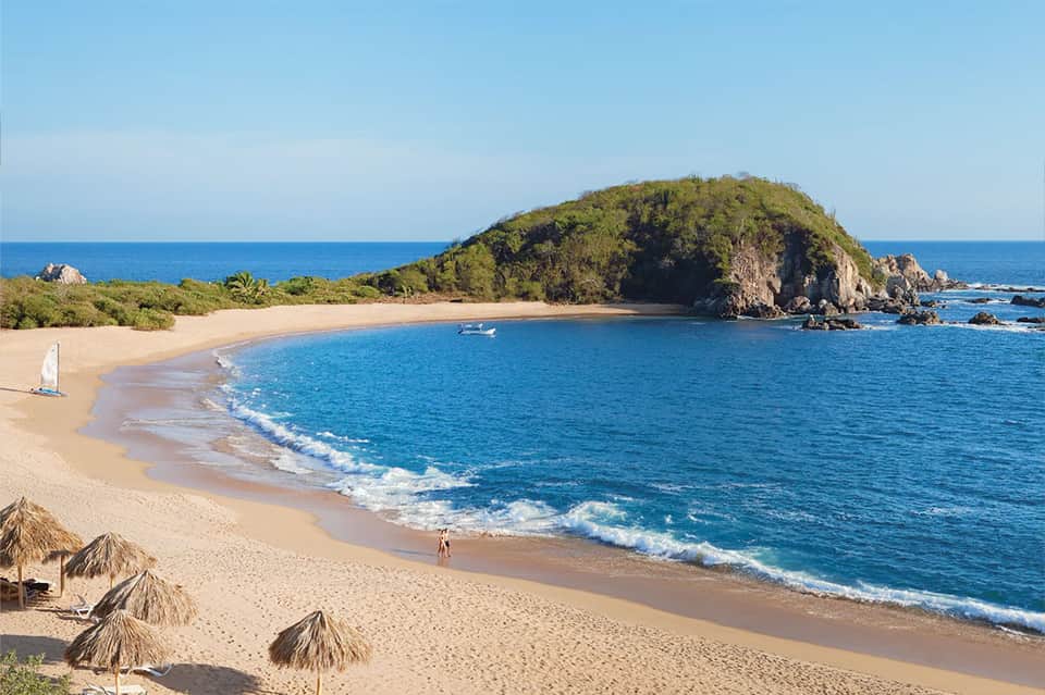 Scenic tropical beach cove with golden sand, turquoise water, lush green hilltop, and gentle waves
