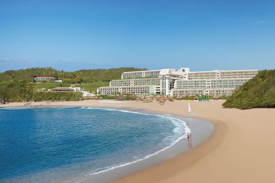 Large beachfront resort hotel on sandy cove surrounded by tropical vegetation