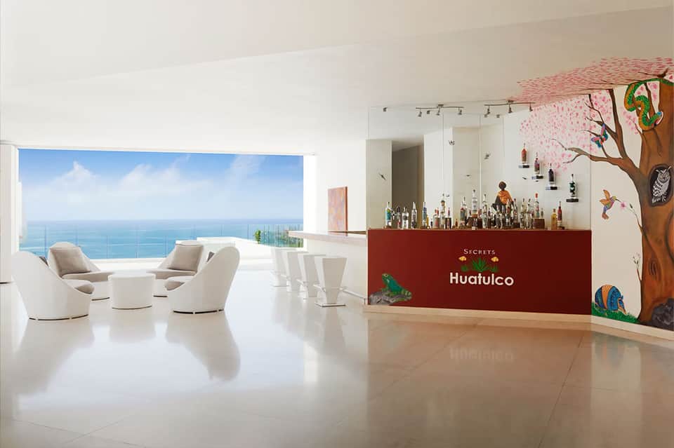 Secrets Huatulco resort lobby with ocean views, white furniture, and tropical-themed bar area