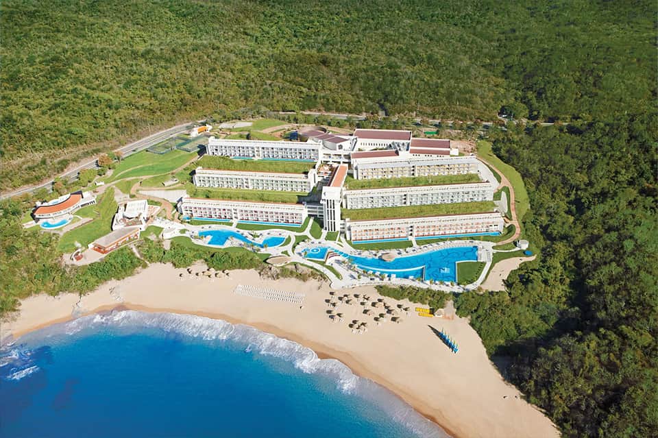 Aerial view of large beachfront resort with multiple pools and buildings nestled in forest