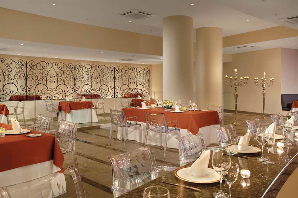 Elegant banquet hall with red tablecloths, ornate wall dividers, chandeliers, and formal table settings