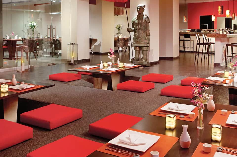 Modern hotel dining space with red cushioned seating, bronze statue, and contemporary design