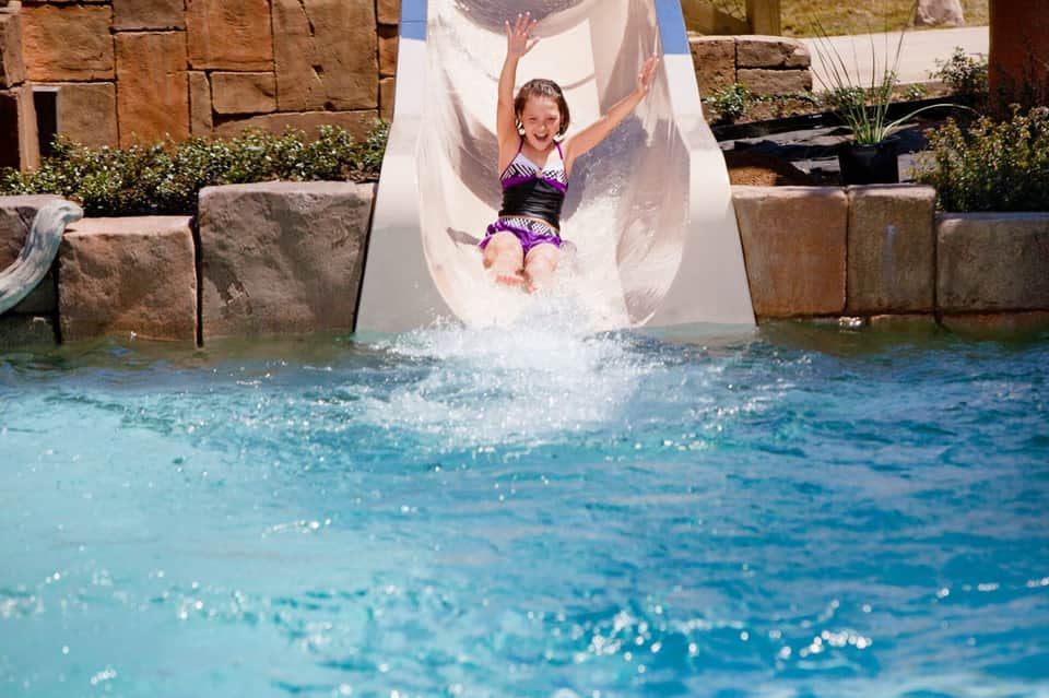 Child sliding down a white water slide into a bright turquoise pool at a resort