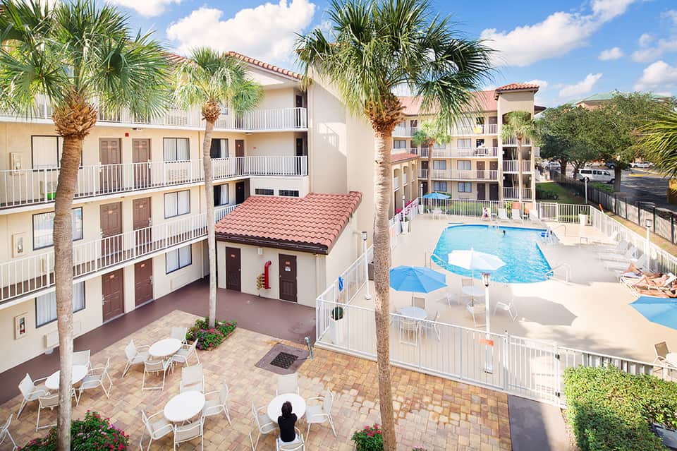 Aerial view of resort courtyard with pool, palm trees, and multi-story beige buildings
