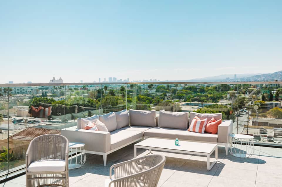 Modern rooftop lounge with sectional seating, glass railings, and expansive city and water views