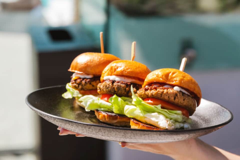 Three gourmet sliders on black plate with fresh vegetables and golden buns