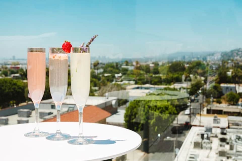 Three champagne cocktails with garnishes on a table overlooking a cityscape
