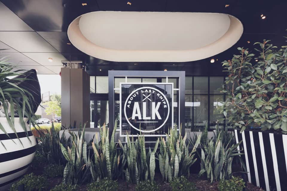 Modern restaurant entrance under curved overhead structure with ALK signage and succulent plants