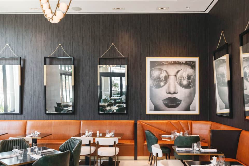Modern restaurant interior with dark wood walls, orange booth seating, mirrors with rope accents, and contemporary art