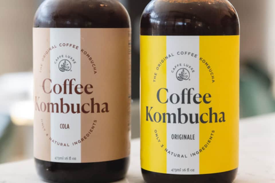 Two bottles of Coffee Kombucha beverages in cola and original flavors on white background