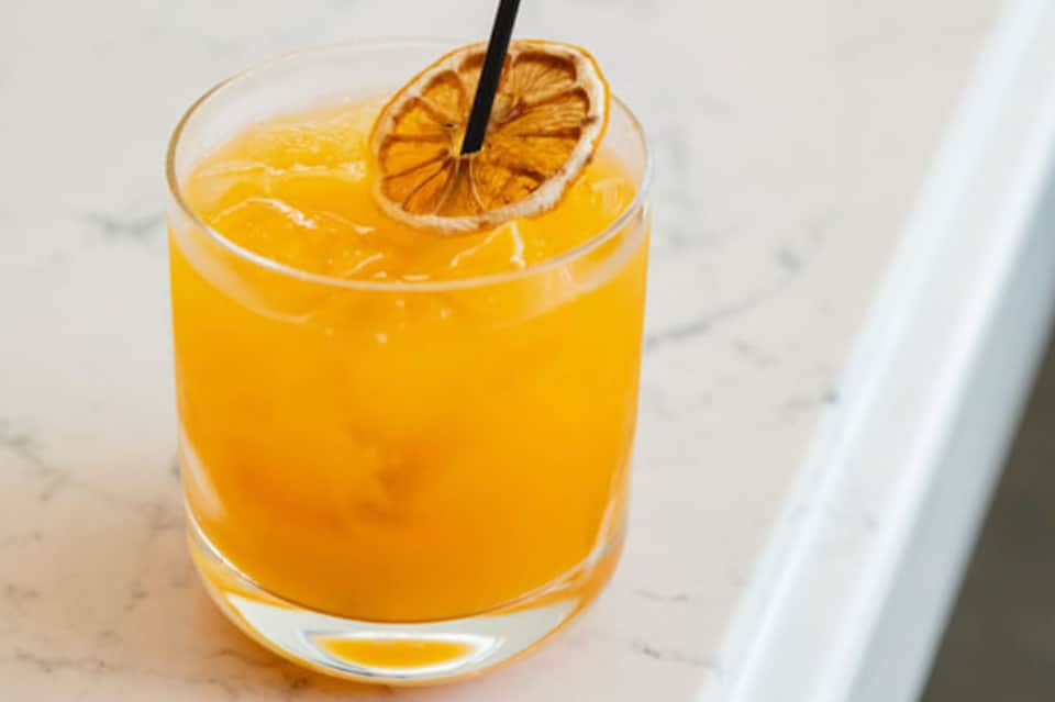 Citrus cocktail with dried orange slice and black straw on white marble surface