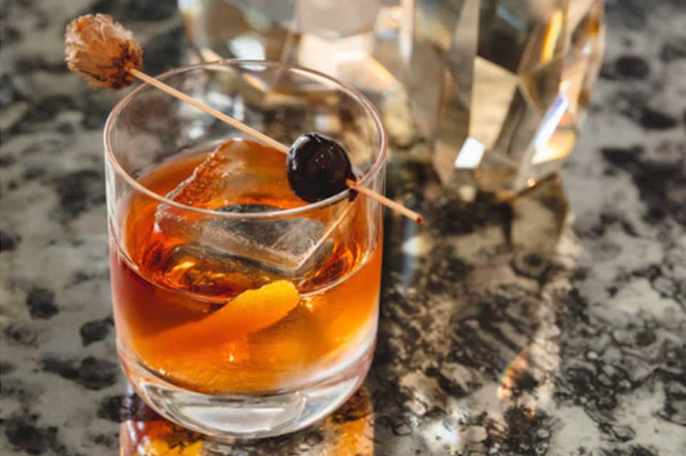 Craft cocktail with orange liqueur, black cherry garnish on stone surface