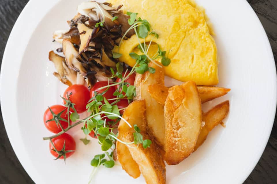 Plated omelet with mushrooms, potatoes, fresh tomatoes, and microgreens on white dish