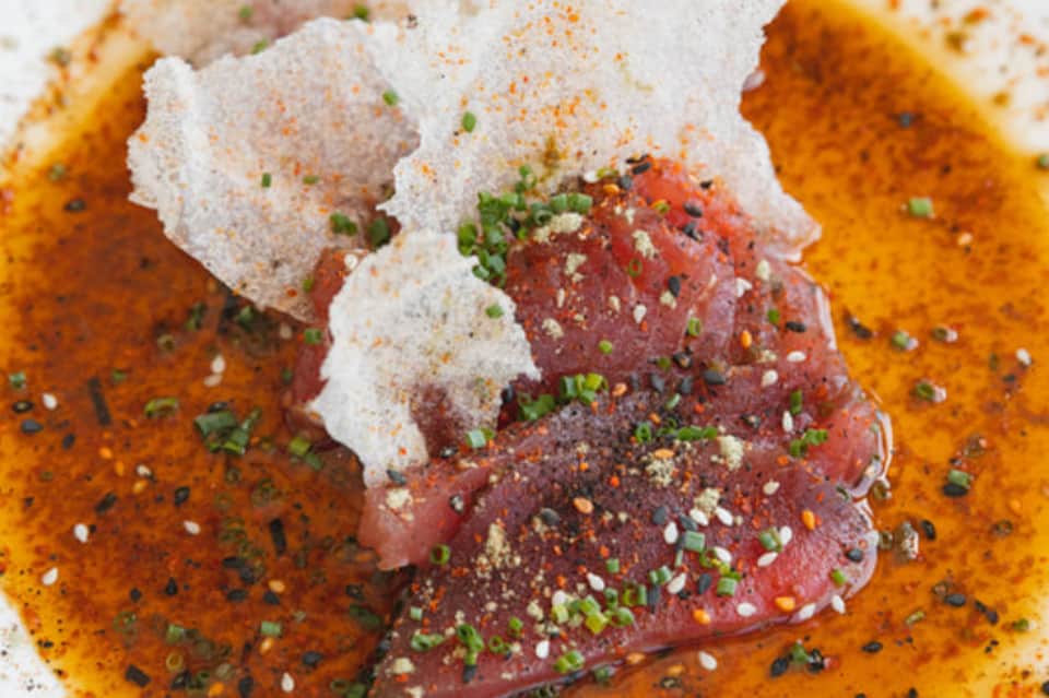 Close-up of seared tuna topped with sesame seeds and herbs on warm sauce