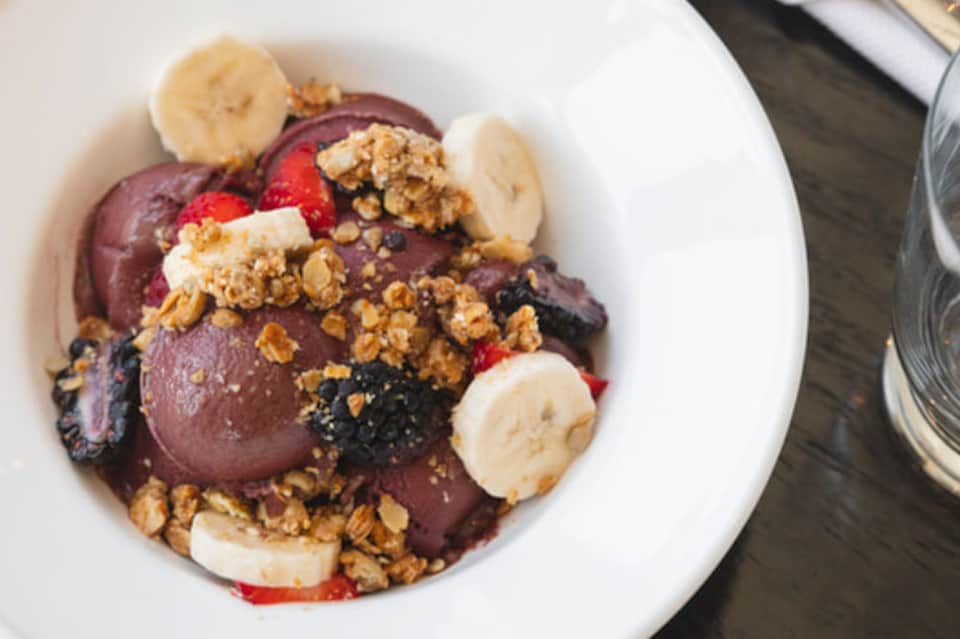Gourmet chocolate ice cream dessert topped with granola, banana slices, and berries on white plate
