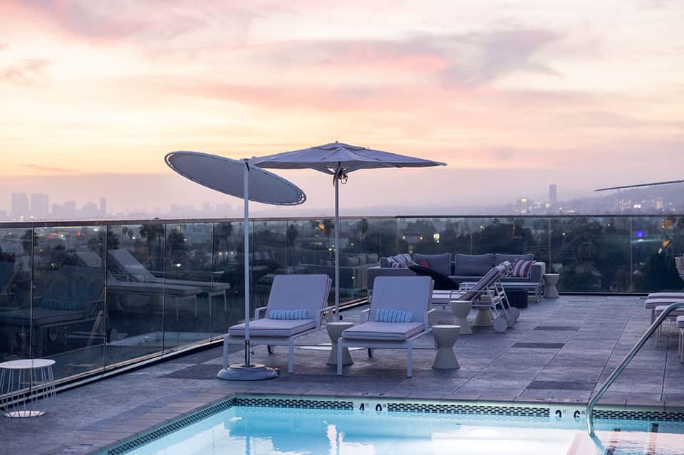 Rooftop terrace at dusk with lounge chairs, umbrellas, and city skyline