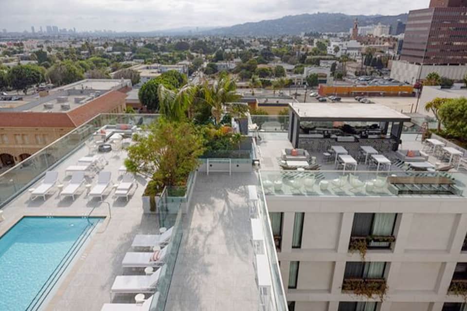 Urban rooftop pool area with lounge chairs, mountain views, and downtown cityscape