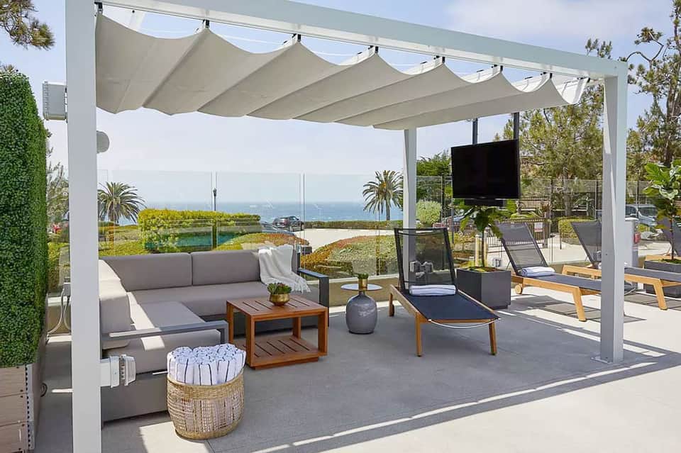 Luxury poolside lounge with white pergola, gray seating, ocean views, and modern landscaping