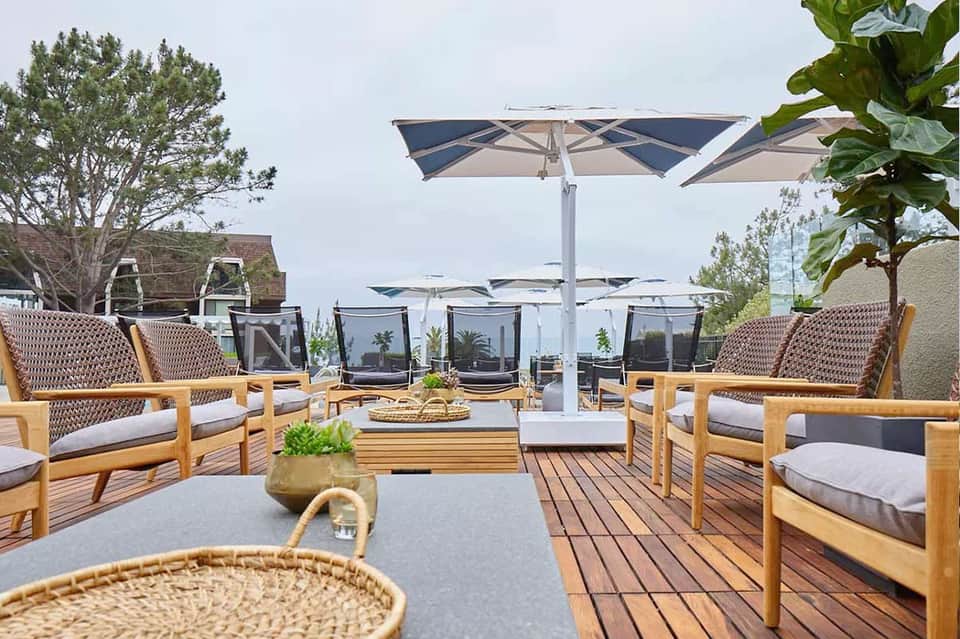 Resort rooftop lounge with wooden chairs, umbrellas, and city views.