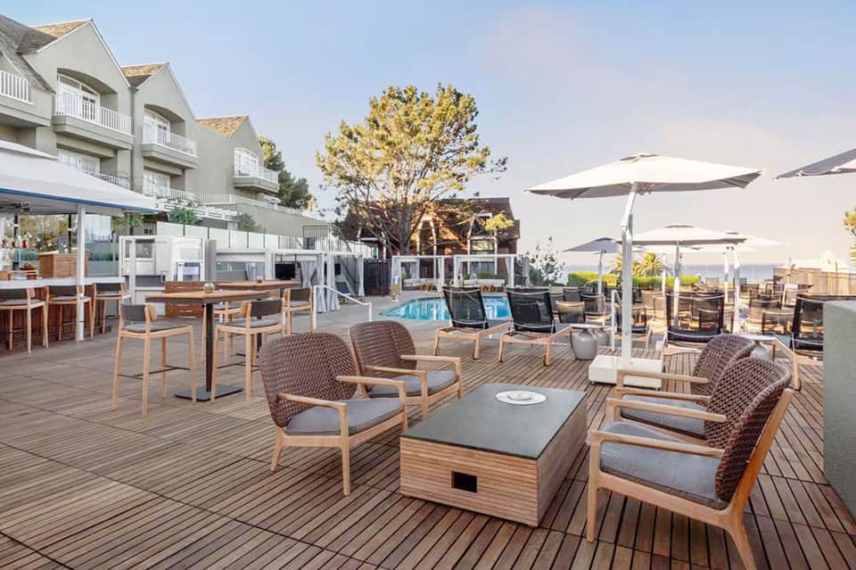 Oceanfront resort terrace with lounge seating, umbrellas, pool and water views at sunset