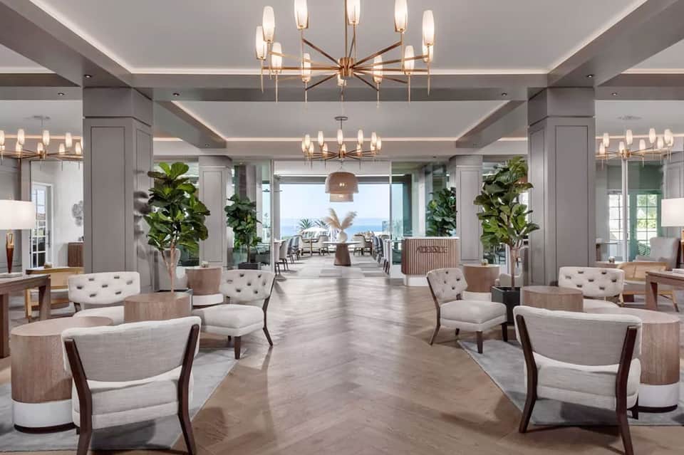 Elegant hotel lobby with marble floors, modern chandeliers, potted plants, and ocean view through windows