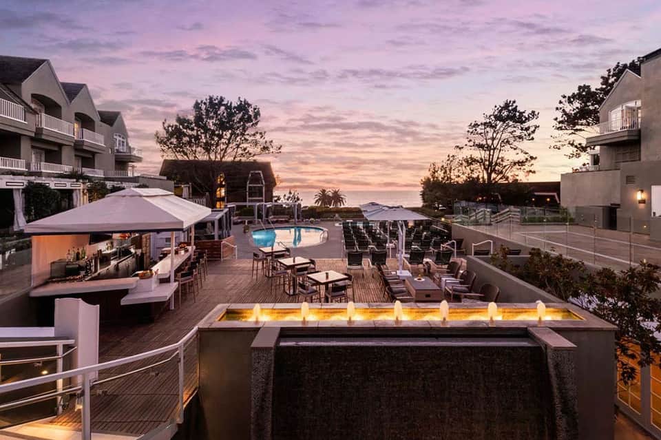 Resort terrace at dusk with fire pit, pool, lounge chairs, and ocean view