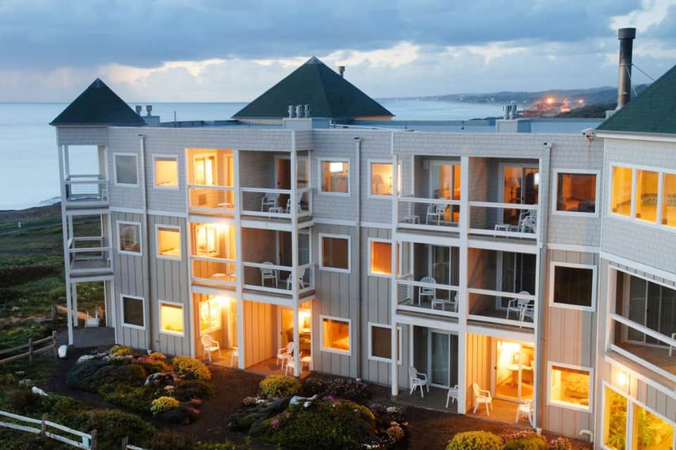 Waterfront resort building with peaked roofs overlooking bay at dusk