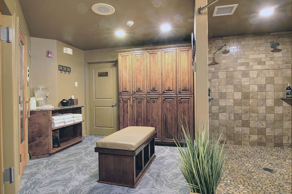 Spa locker room with wooden lockers, massage table, towel storage, and large tiled shower area