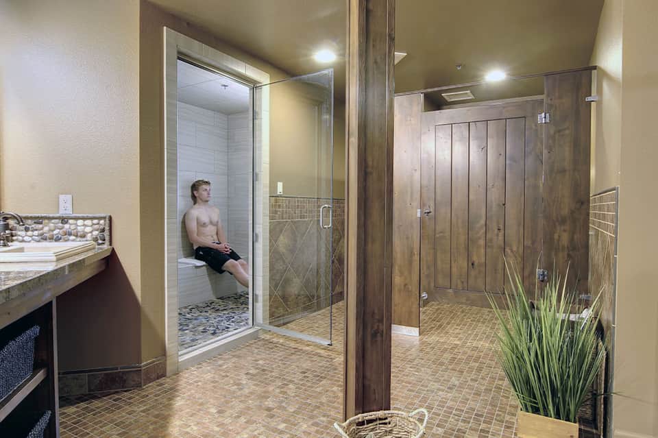 Large spa bathroom with two modern showers, glass enclosures, neutral tile flooring, vanity sink, and wood accents.
