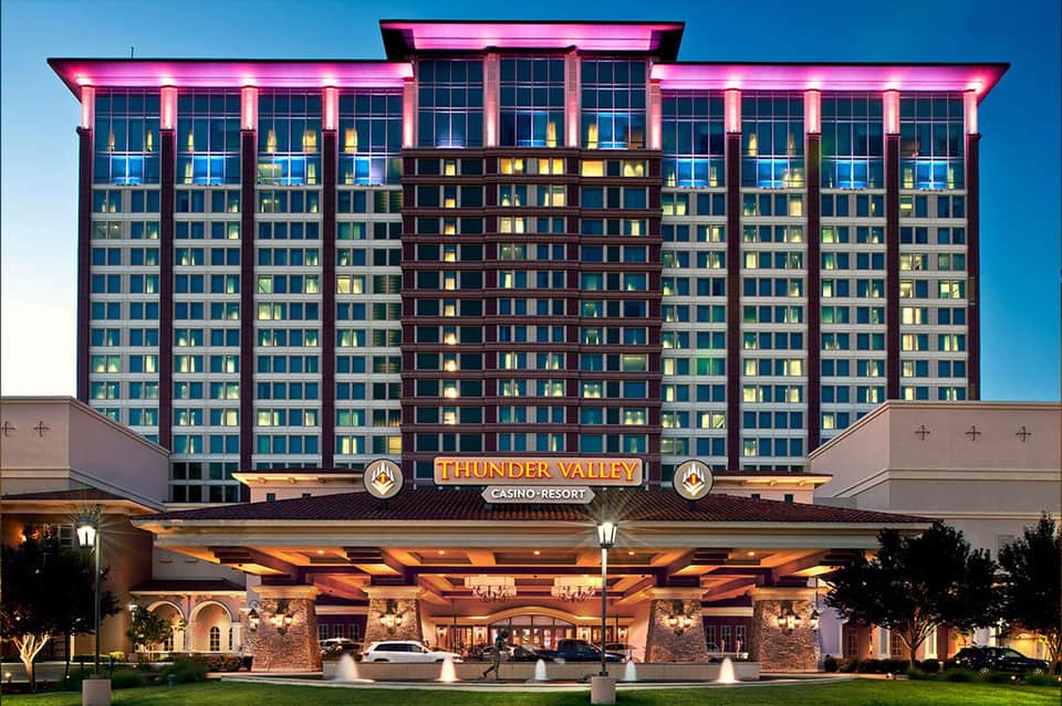 Illuminated casino resort hotel at dusk with magenta neon lighting on building exterior and lighted plaza