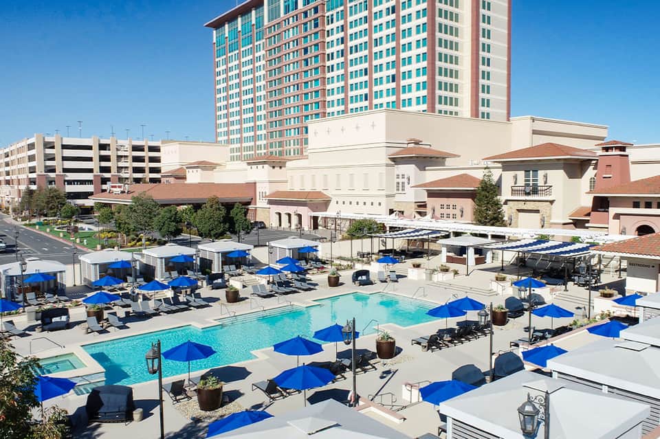 Resort pool deck with blue umbrellas, lounge chairs, and high-rise hotel building