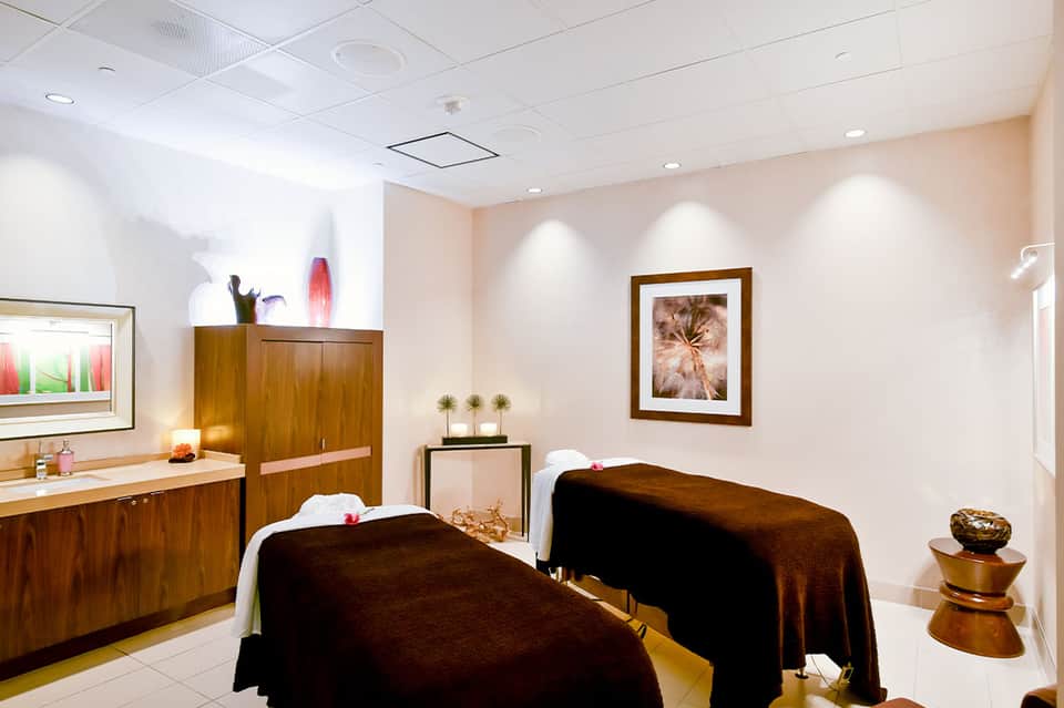 Spa treatment room with two massage tables, wooden cabinetry, and framed botanical artwork