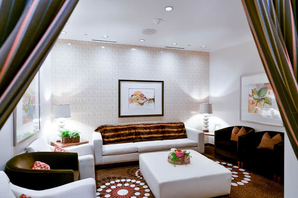 Elegant hotel lounge with white sofa, black chairs, patterned carpet, and botanical artwork on neutral walls