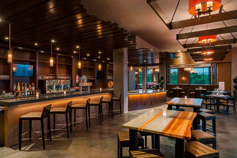 Modern resort bar and restaurant interior with wood accents, pendant lighting, and floor-to-ceiling windows