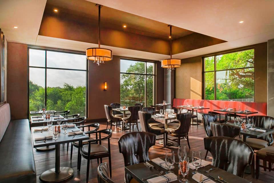Modern restaurant interior with large windows, dark leather chairs, and forest views