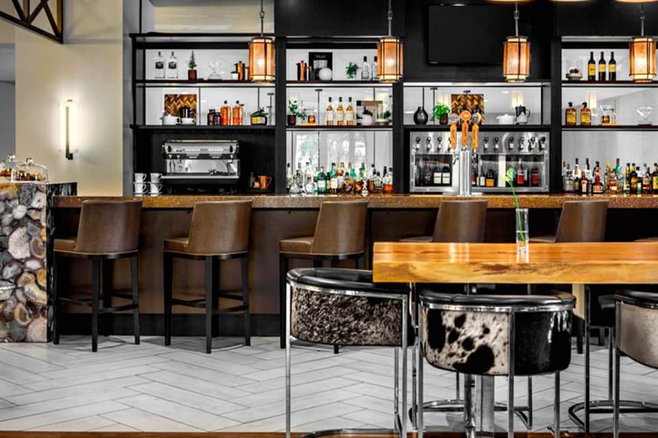 Modern bar with black and white shelving displaying bottles, wood countertops, and cow-print bar stools