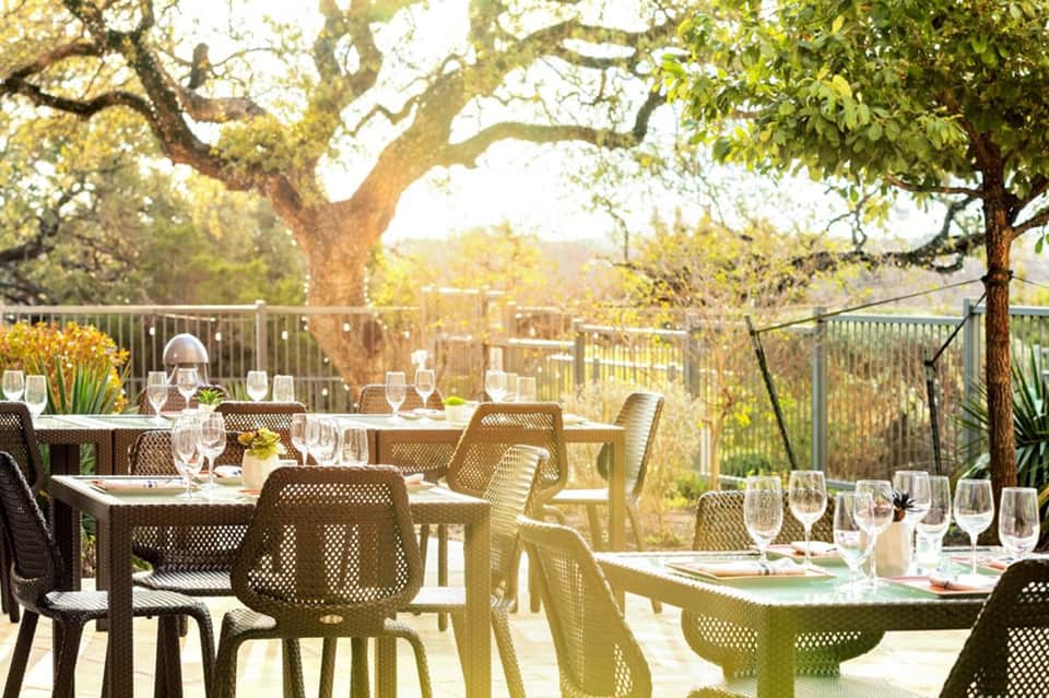 Outdoor dining terrace under large oak trees with place settings and views