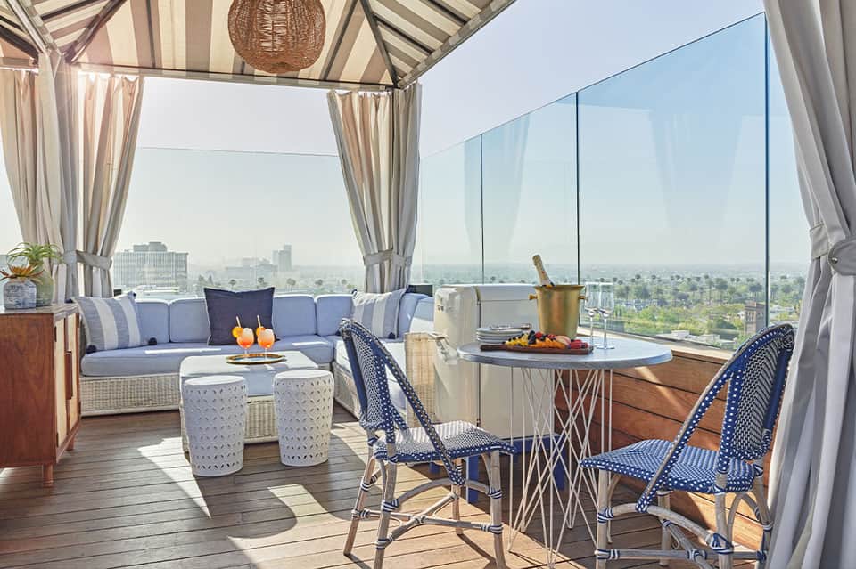 Luxury rooftop lounge with blue seating, striped awning, city skyline views, and champagne