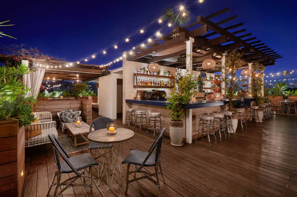 Rooftop bar with pergola, string lights, full bar, and twilight city skyline