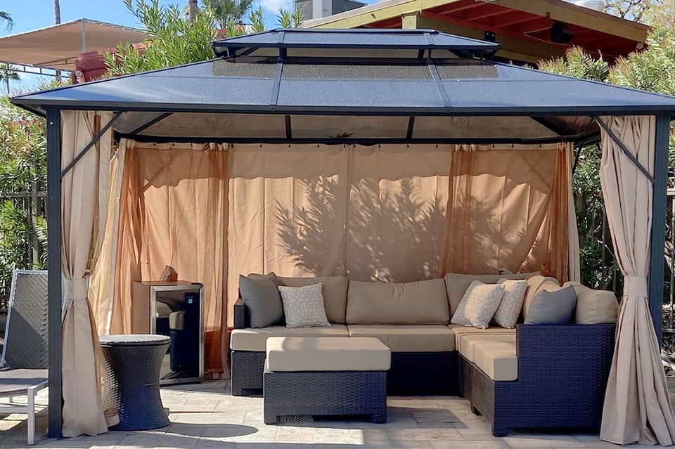 Modern gazebo with dark metal frame, beige curtains, and comfortable lounge seating