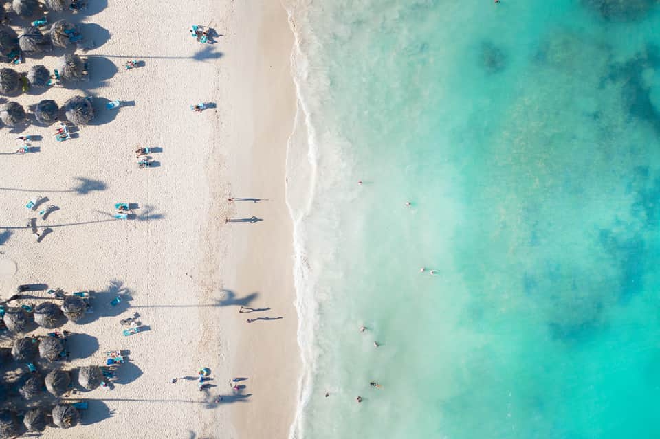 Aerial view of pristine white sand beach with turquoise water, boats, and beach umbrellas