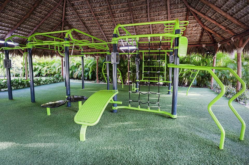 Bright green outdoor fitness equipment under thatched roof with tropical garden surroundings
